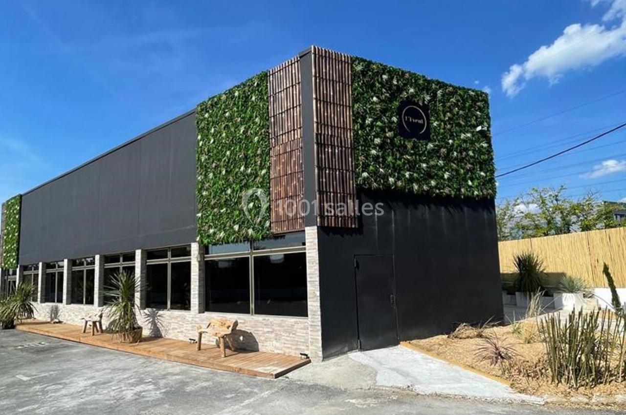 Façade d'un bâtiment moderne avec un mur végétal, des panneaux en bois et une terrasse en bois, sous un ciel bleu.