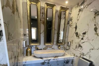 Salle de bain avec lavabo en pierre, trois miroirs dorés rectangulaires et murs en marbre aux motifs noirs et blancs.