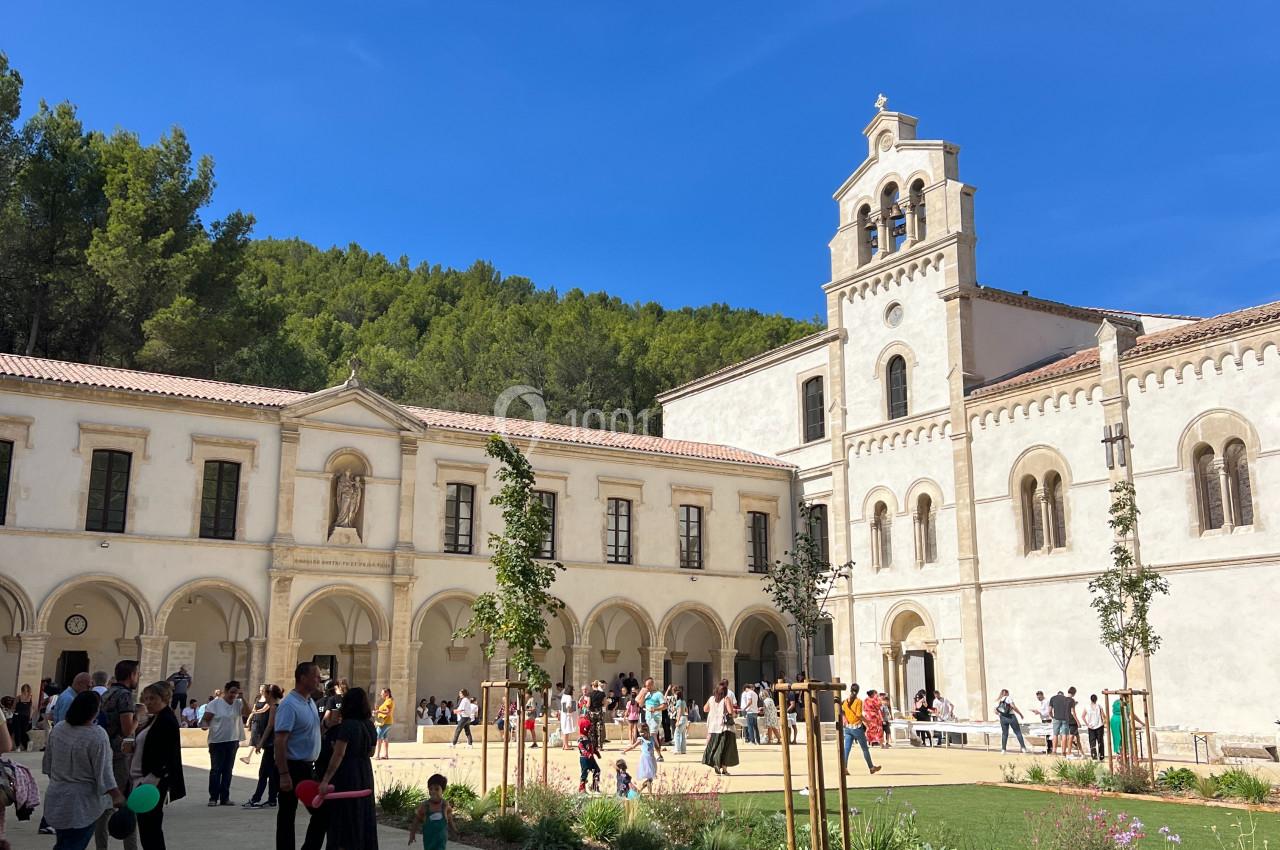 Personnes rassemblées dans la cour d'un bâtiment religieux avec clocher, entouré de végétation sous un ciel bleu.
