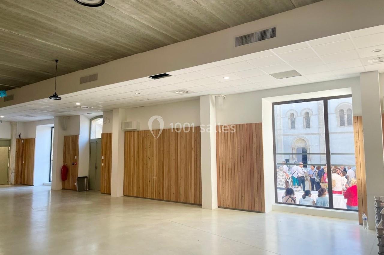 Salle intérieure lumineuse avec murs en bois, sol clair et grande fenêtre donnant sur une scène extérieure animée.