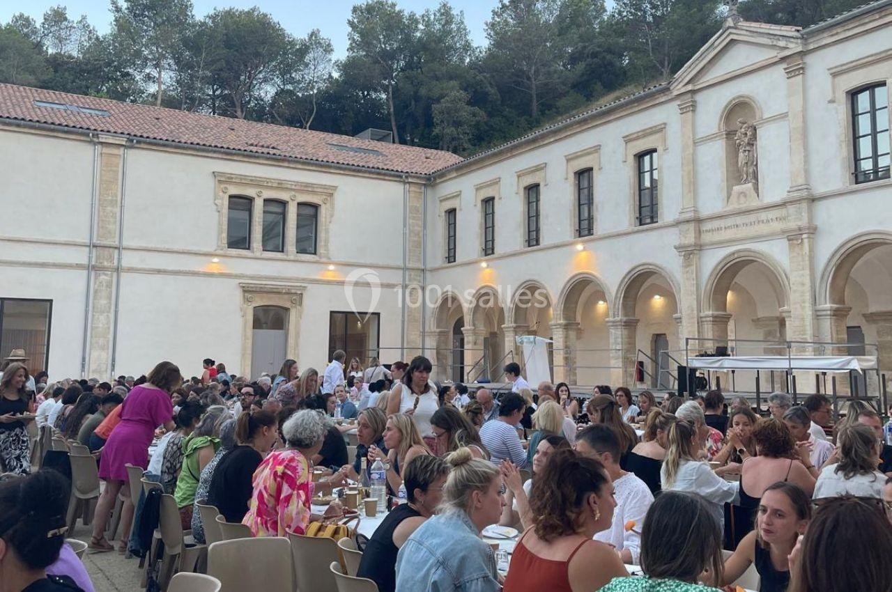 Groupe de personnes dînant en plein air dans la cour d'un bâtiment historique entouré d'arcades et de végétation.