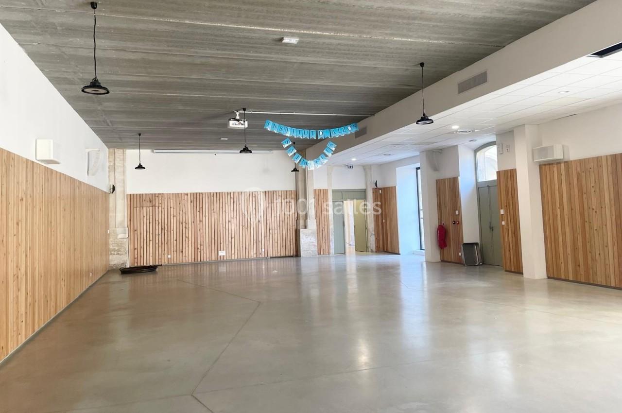 Salle vide avec murs en bois clair, sol en béton, plafond en béton brut et guirlande bleue suspendue.