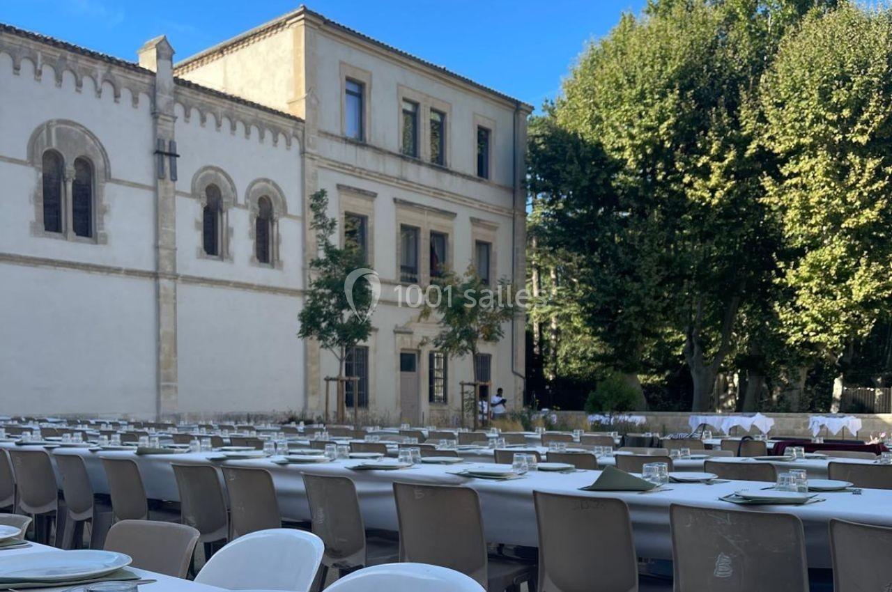 Tables dressées en extérieur avec assiettes et couverts, devant un bâtiment ancien entouré d'arbres.