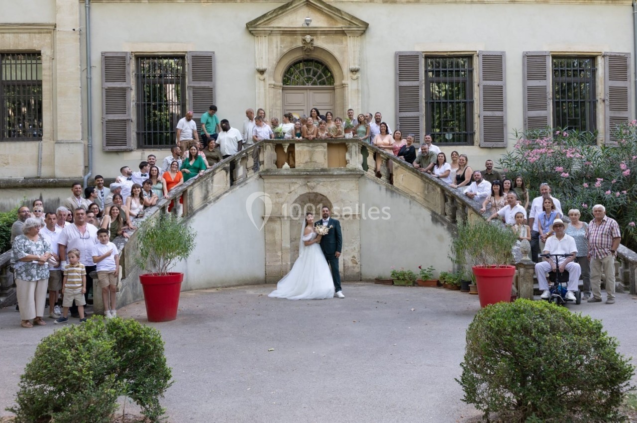 Un couple de mariés pose sur un escalier entouré de nombreux invités devant un bâtiment ancien.