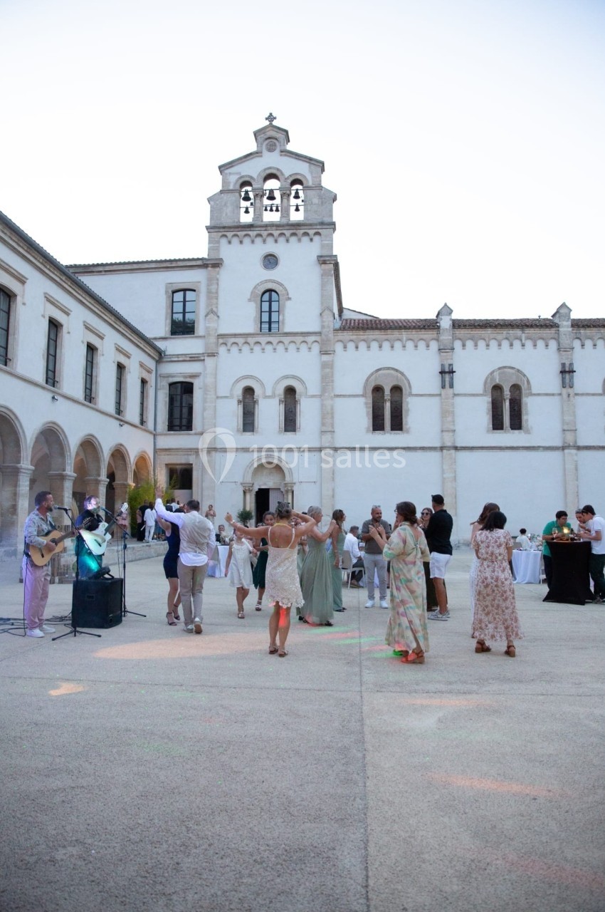 Groupe de personnes dansant en plein air dans la cour d'un bâtiment historique blanc au crépuscule.