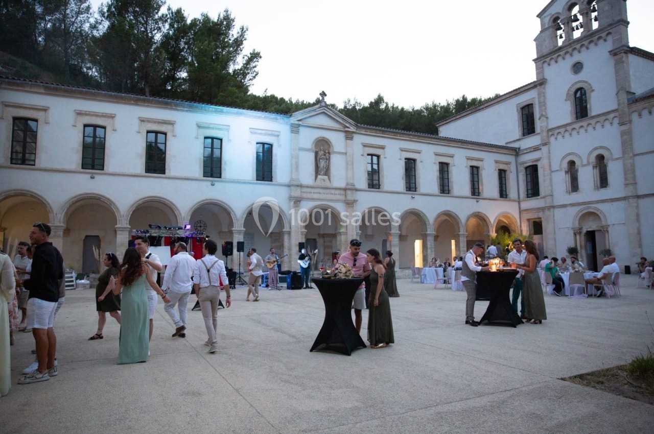 Personnes rassemblées dans la cour d'un bâtiment historique avec arcades, lors d'un événement en soirée.