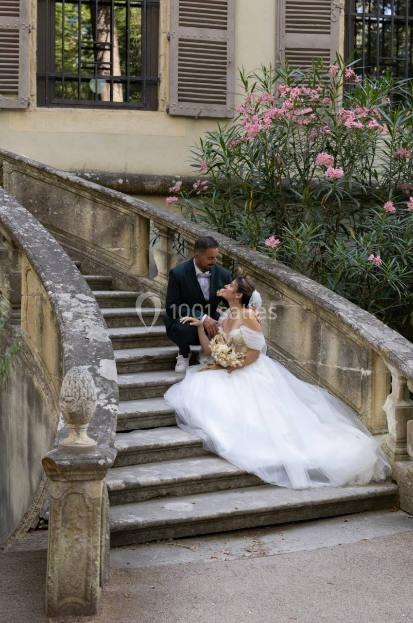 Un couple de mariés assis sur un escalier en pierre, entouré de fleurs et d'une végétation luxuriante.