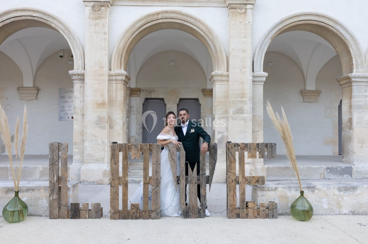Un couple en tenue de mariage pose devant des arches en pierre et des lettres formant le mot ’LOVE’.