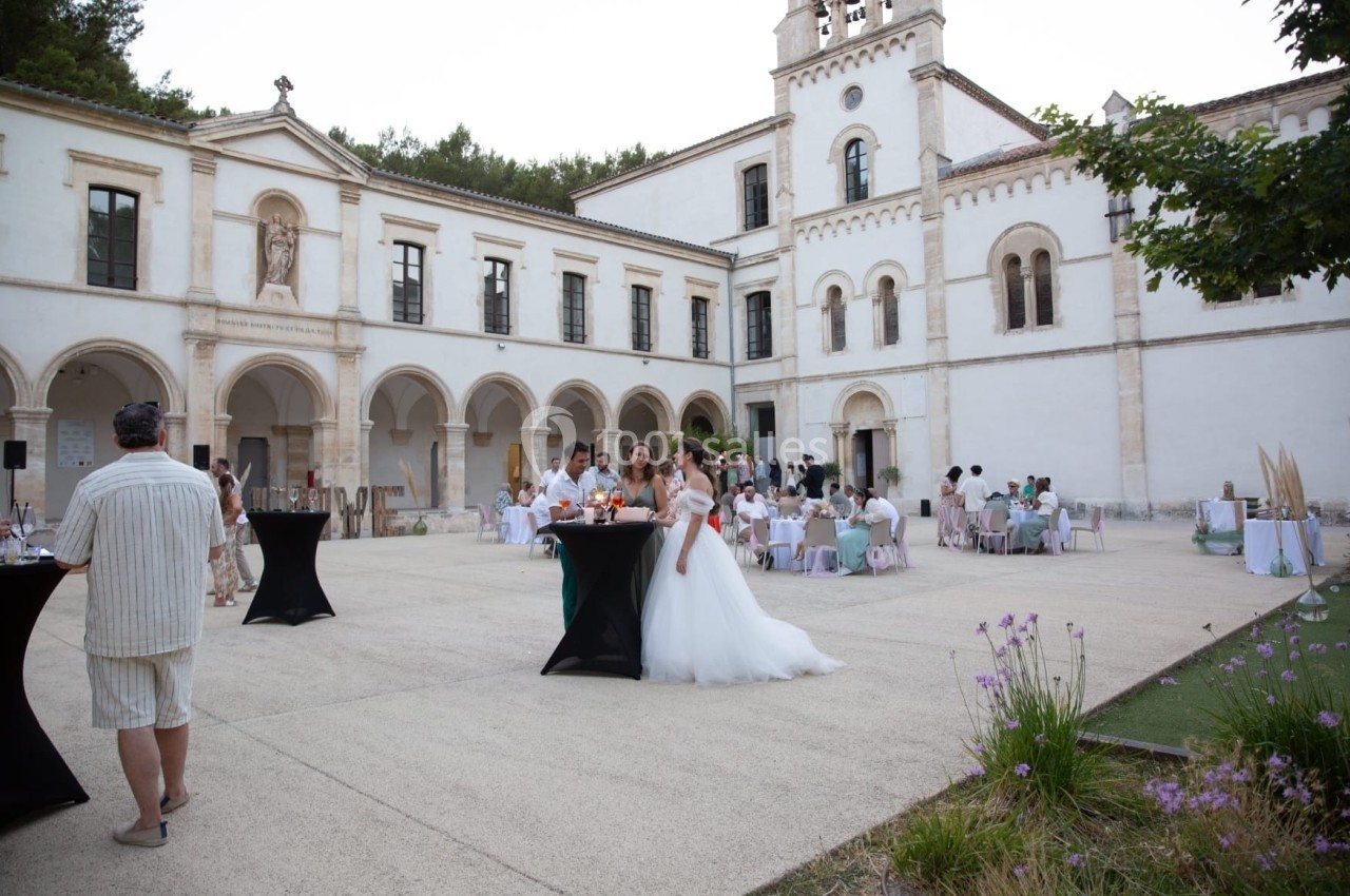 Mariage en plein air dans la cour d'un bâtiment historique, avec invités autour de tables et mariée en robe blanche.