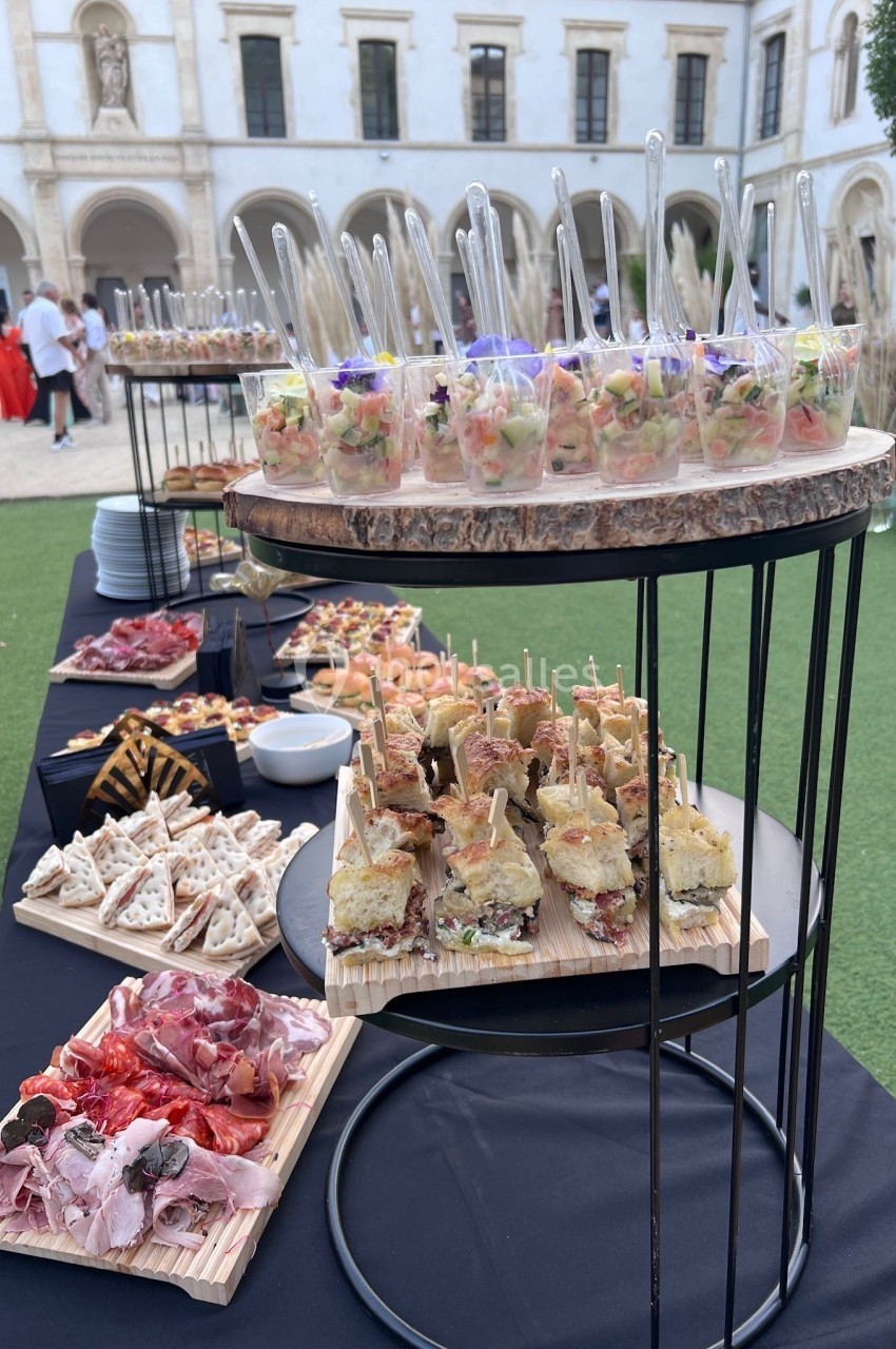 Buffet en plein air avec verrines, sandwichs, charcuterie et amuse-bouches, disposés sur des tables dans une cour.
