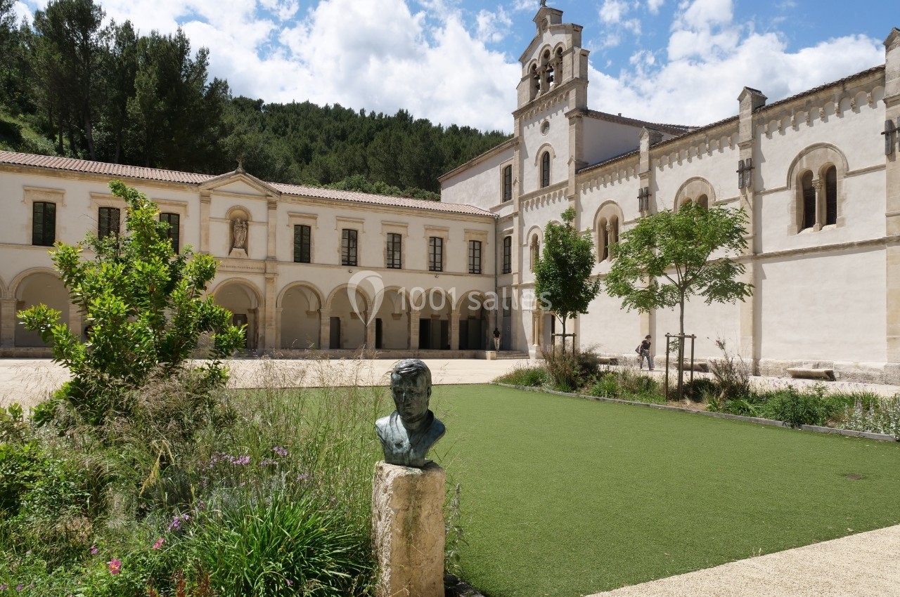 Cour intérieure d'un monastère avec pelouse, statue en buste au premier plan et bâtiments historiques en arrière-plan.
