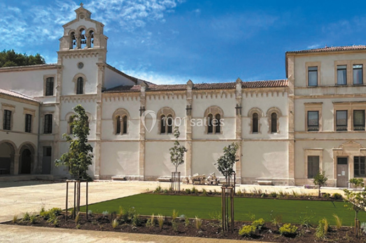 Façade d'un bâtiment historique blanc avec une cour aménagée de pelouse, d'arbustes et d'arbres jeunes.