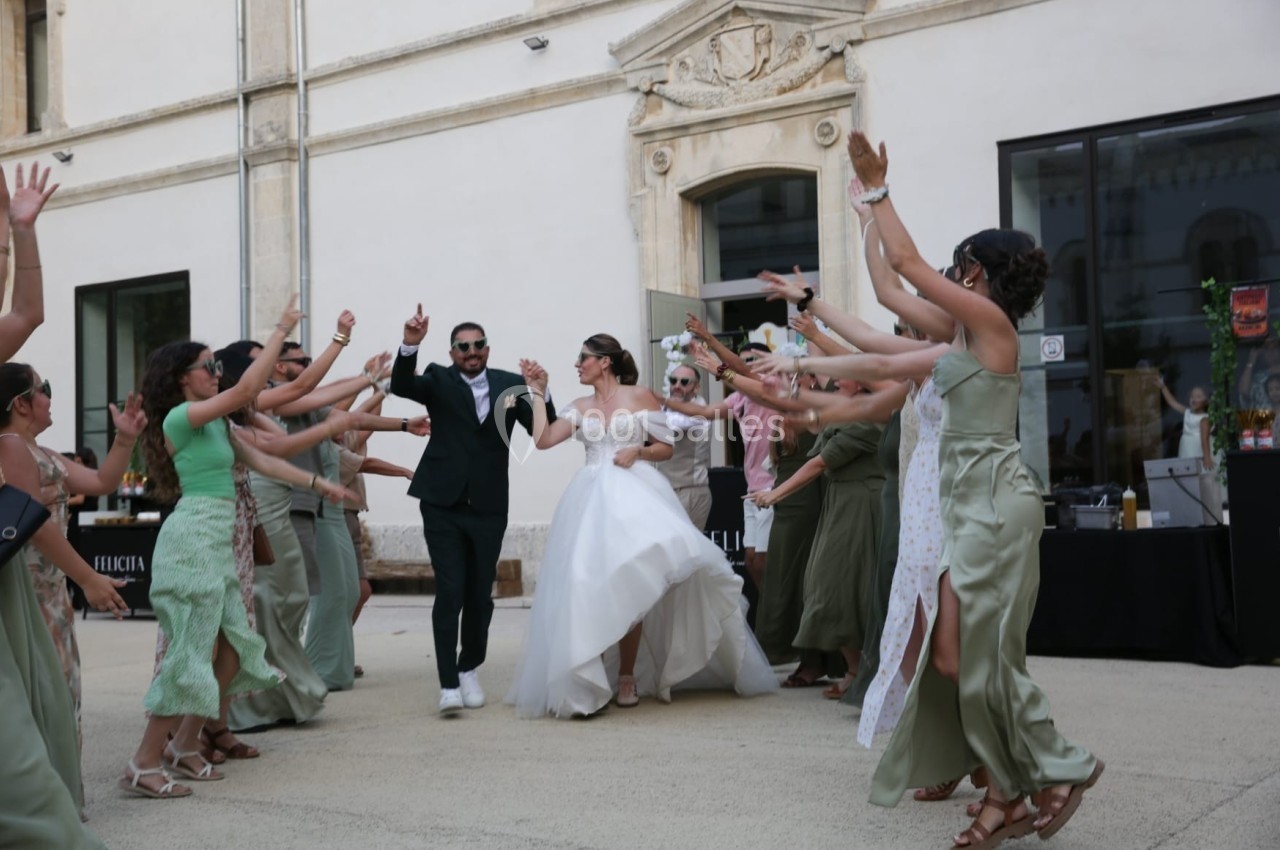 Un couple de mariés danse entouré d'invités en tenue festive dans une cour extérieure.
