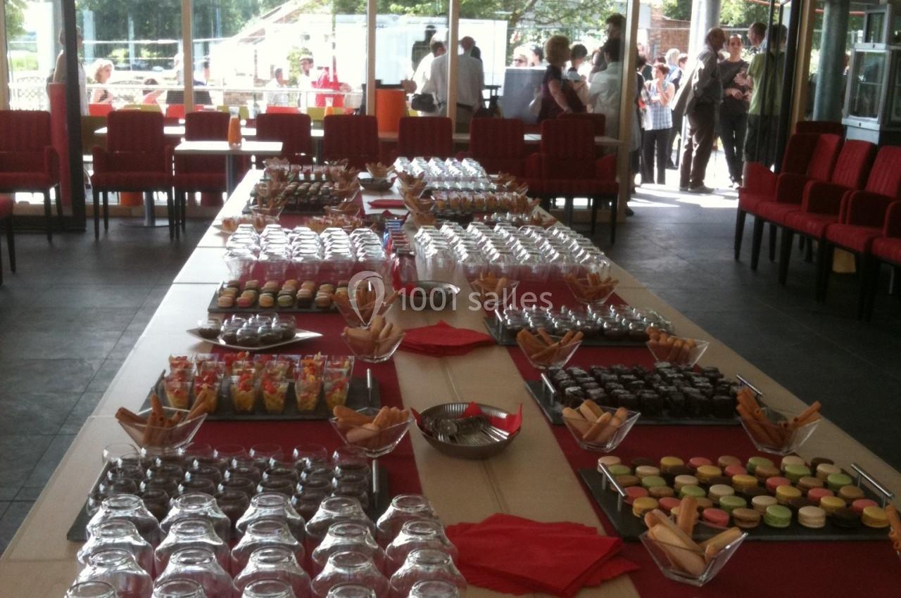 Tables garnies de desserts variés, verrines, macarons et pâtisseries, disposées pour un buffet dans une salle lumineuse.