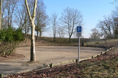 Parking vide en plein air entouré d'arbres, avec un panneau indiquant une zone de stationnement.