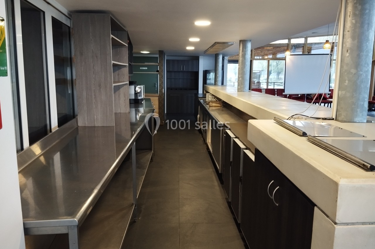 Cuisine professionnelle avec plans de travail en inox, étagères ouvertes, réfrigérateurs et éclairage naturel.