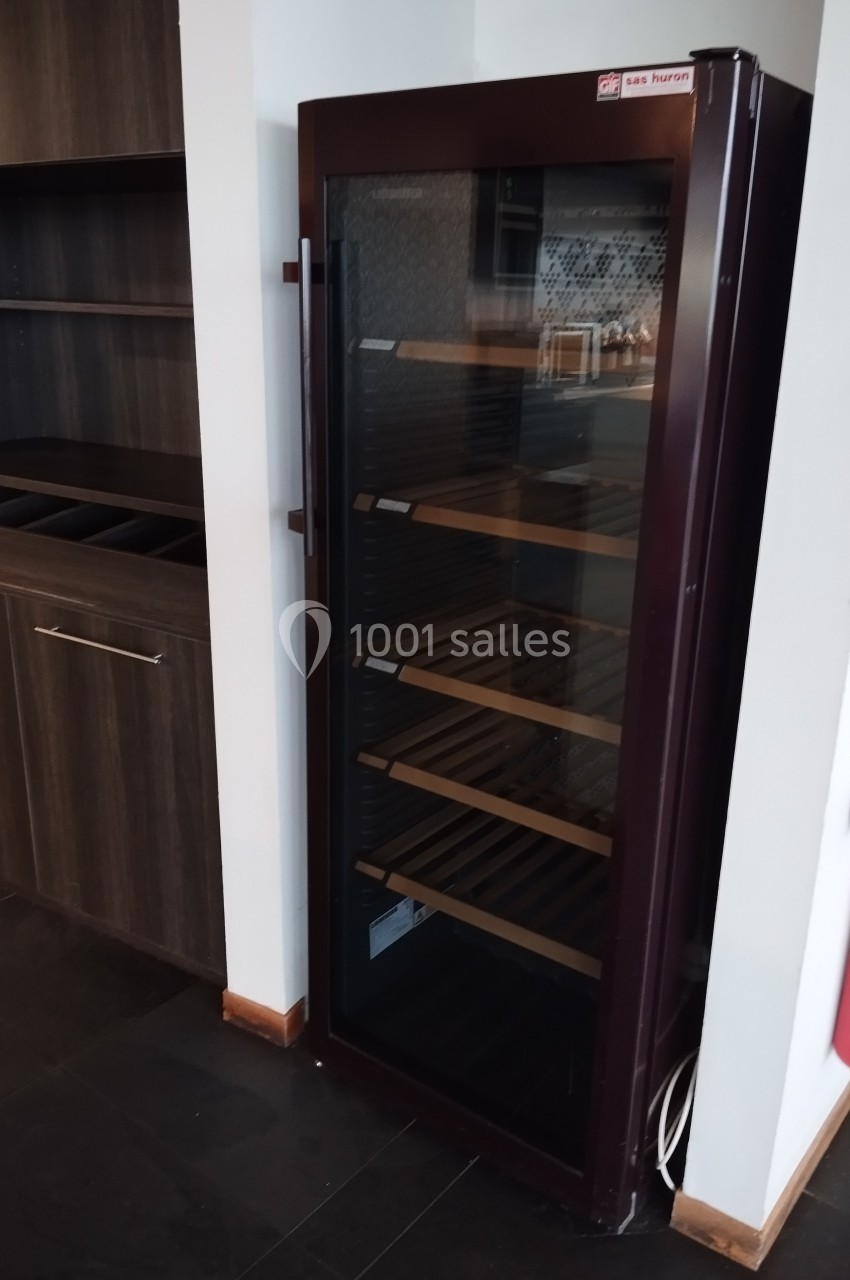 Armoire à vin vitrée avec étagères en bois, placée dans un coin d'une pièce avec des meubles en bois sombre.