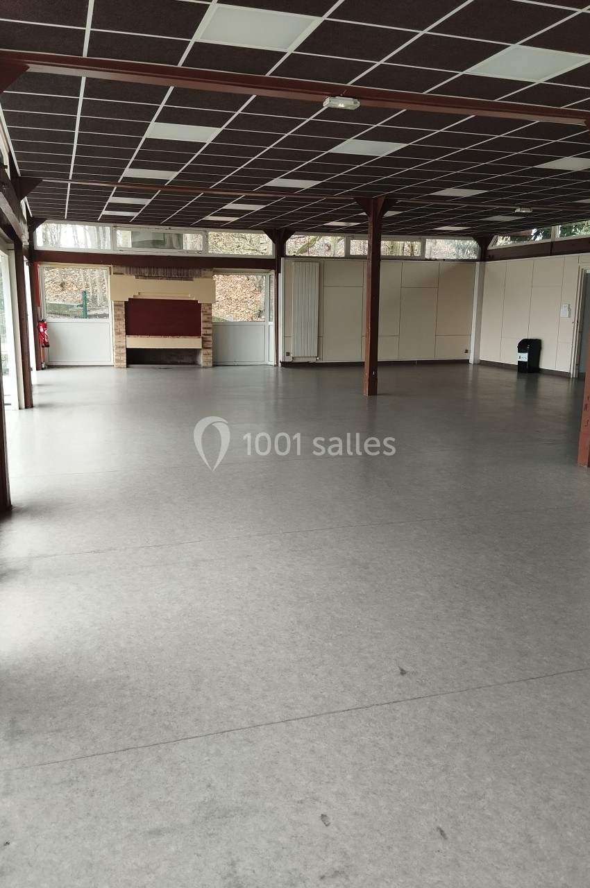 Salle vide avec sol en lino gris, plafond à dalles noires et blanches, murs clairs et cheminée en fond.