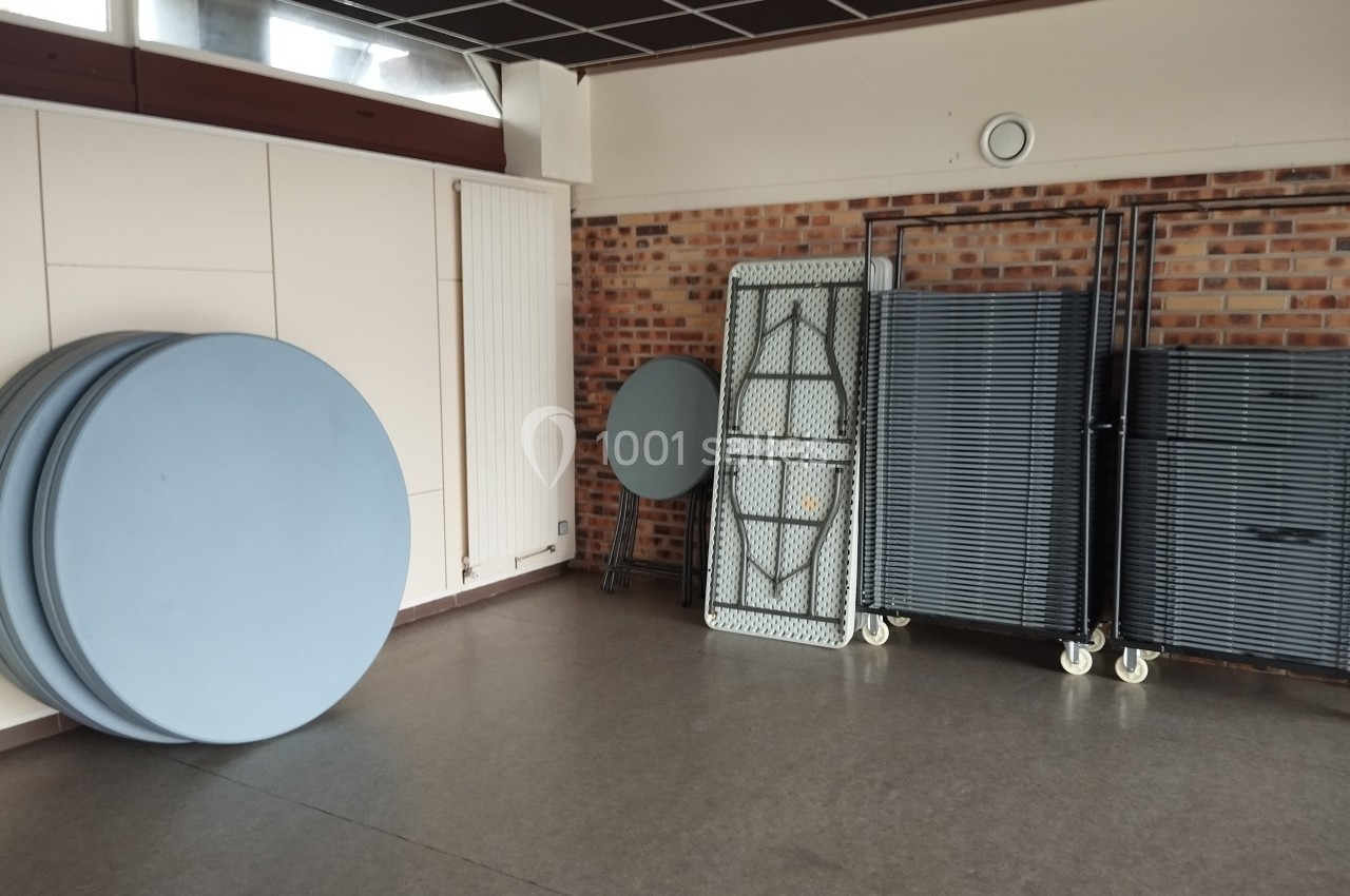 Tables rondes et rectangulaires pliées et empilées contre un mur dans une salle au sol en linoléum.