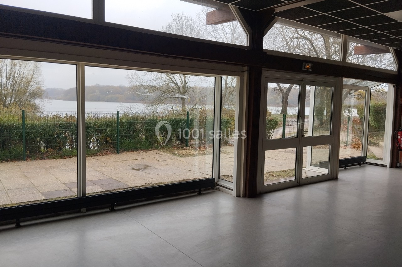 Vue intérieure d'une salle avec de grandes baies vitrées donnant sur un paysage extérieur arboré et un plan d'eau.