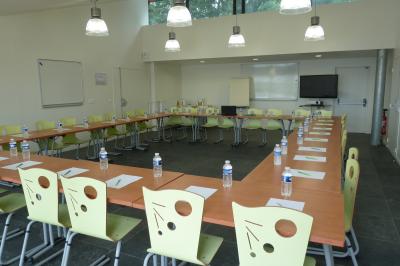 Bâtiment en briques avec de grandes baies vitrées, entouré d'arbres, près d'un plan d'eau sous un ciel dégagé.