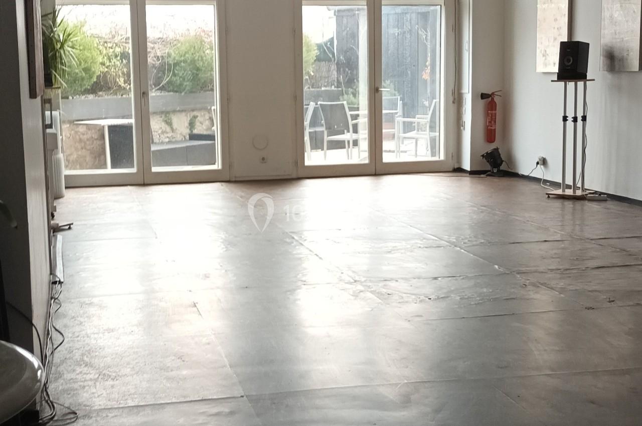 Salle lumineuse avec un sol en béton, des murs blancs, une grande baie vitrée et une boule disco suspendue.