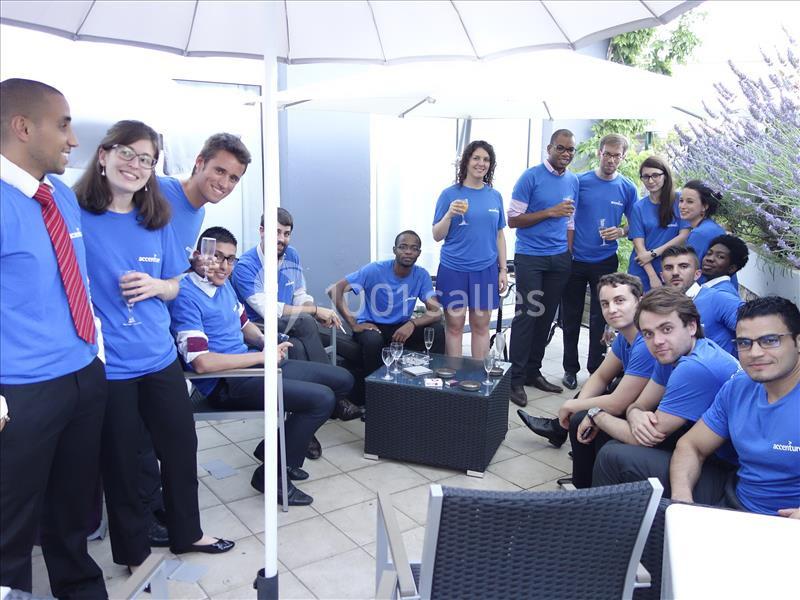 Un groupe de personnes en t-shirts bleus discute et partage un moment convivial sur une terrasse sous des parasols.