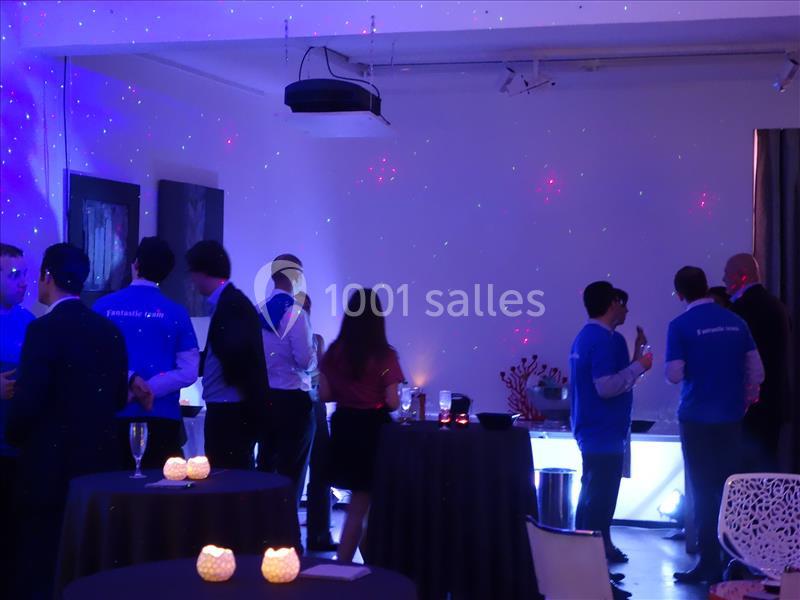 Groupe de personnes discutant dans une salle faiblement éclairée avec des lumières colorées et des tables hautes.