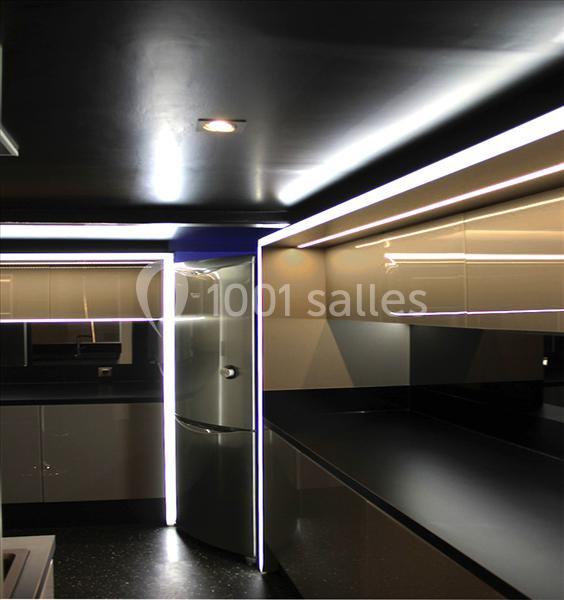 Cuisine moderne avec éclairage LED intégré, meubles noirs et blancs brillants, et réfrigérateur argenté.