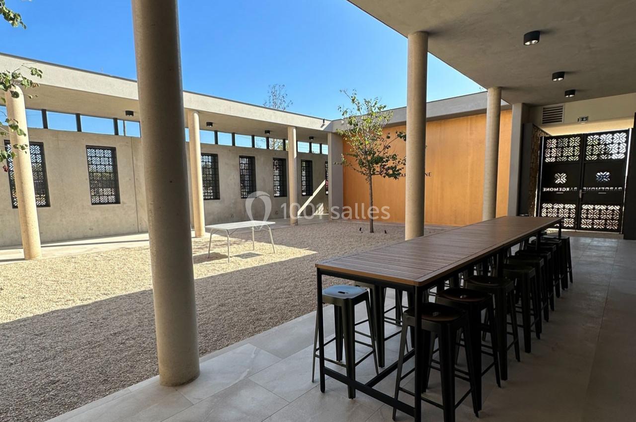 Cour intérieure moderne avec tables hautes, tabourets, sol en gravier et murs ornés de motifs ajourés.