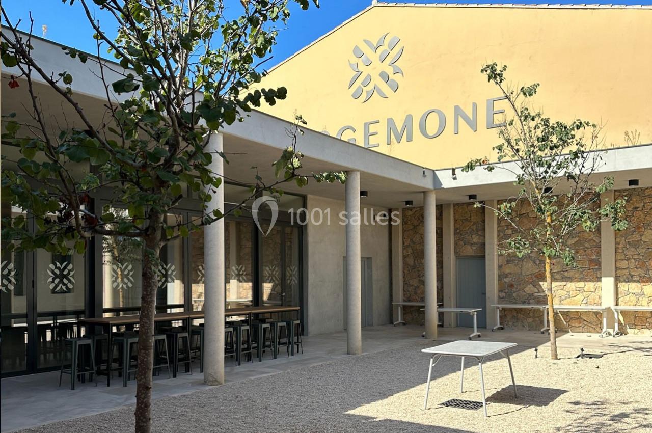 Cour extérieure avec tables, arbres et façade d’un bâtiment beige portant l’inscription ’CEMONE’.