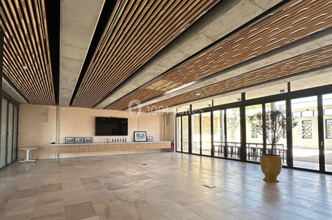 Salle lumineuse avec plafond en bois, murs vitrés, sol en pierre et mobilier minimaliste, incluant une plante en pot.