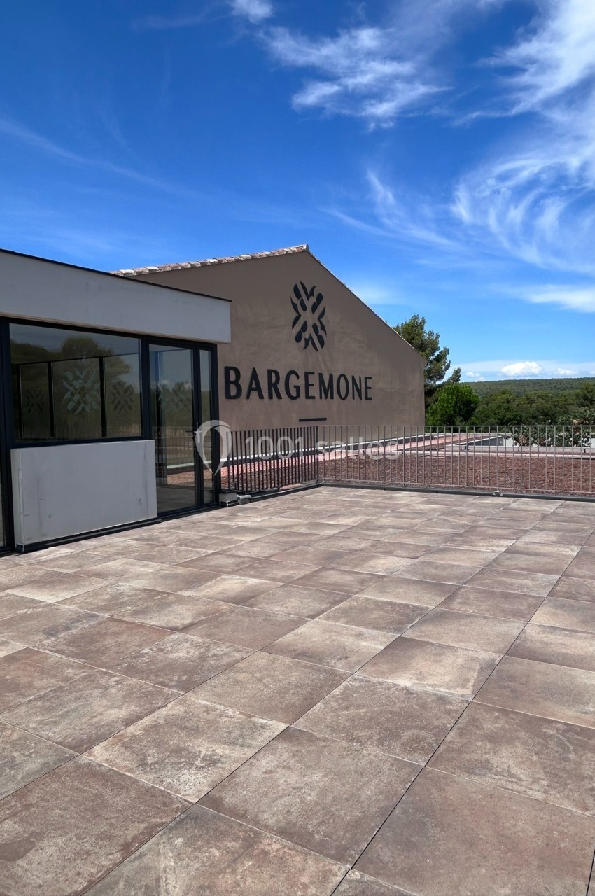 Terrasse en pierre avec vue sur un bâtiment beige marqué ’Bargemone’ et un paysage naturel en arrière-plan.