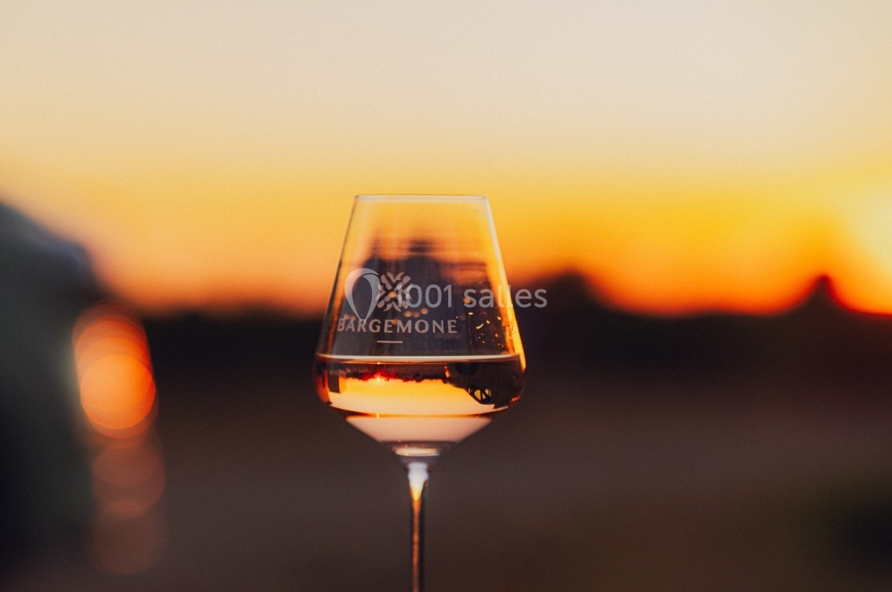 Verre de vin rosé sur fond de coucher de soleil, avec un logo gravé sur le verre.
