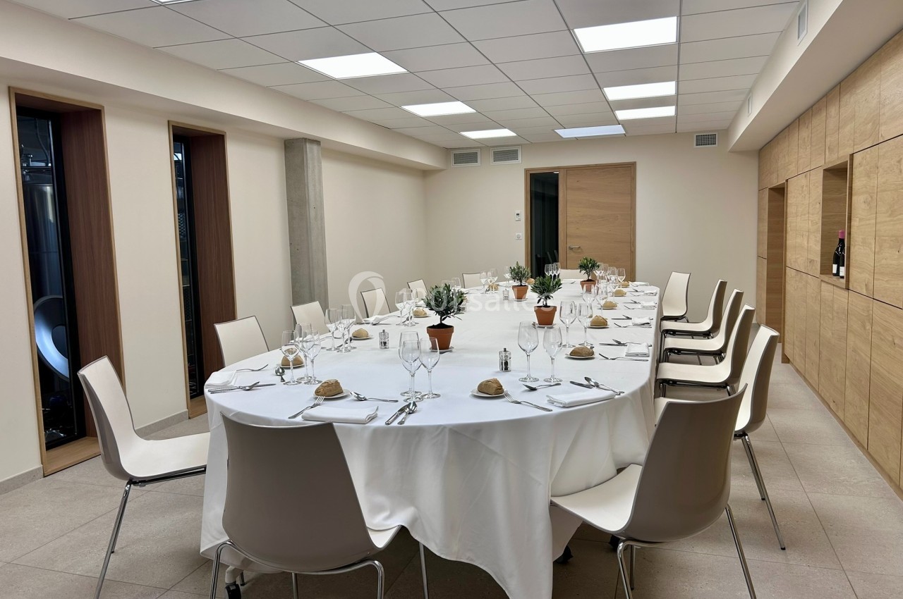 Salle de réception moderne avec une grande table ronde dressée, entourée de chaises blanches.