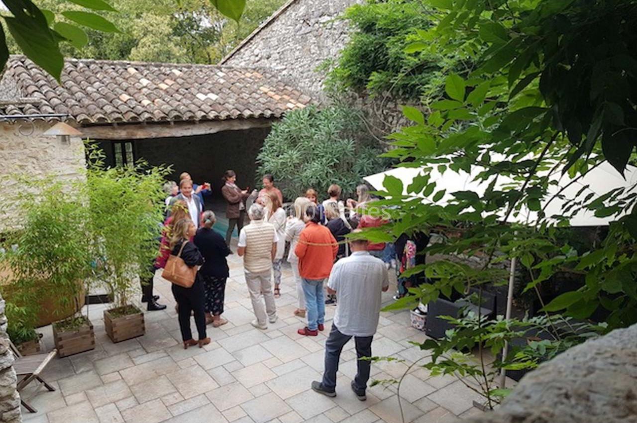 Un groupe de personnes discute dans une cour pavée entourée de végétation et de bâtiments en pierre.