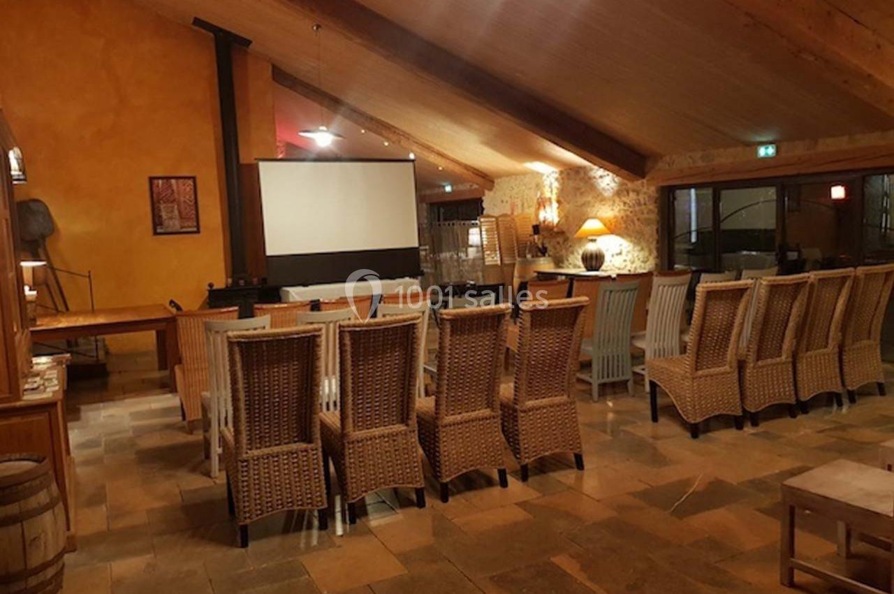 Salle avec des chaises en osier disposées face à un écran de projection dans un espace au plafond en bois.