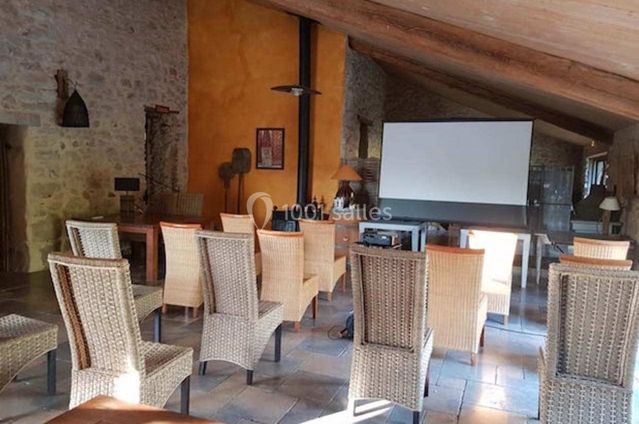 Salle de réunion avec des chaises en osier disposées face à un écran de projection dans un espace en pierre et bois.