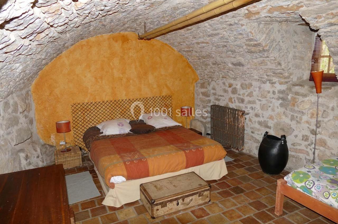 Chambre rustique avec murs en pierre, lit double, petite fenêtre, sol en carreaux et mobilier simple.