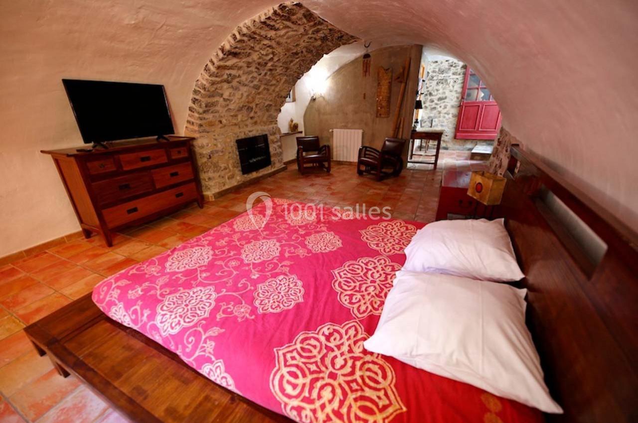 Chambre voûtée avec lit double, couvre-lit rouge à motifs, mobilier en bois, téléviseur et sol en carreaux.