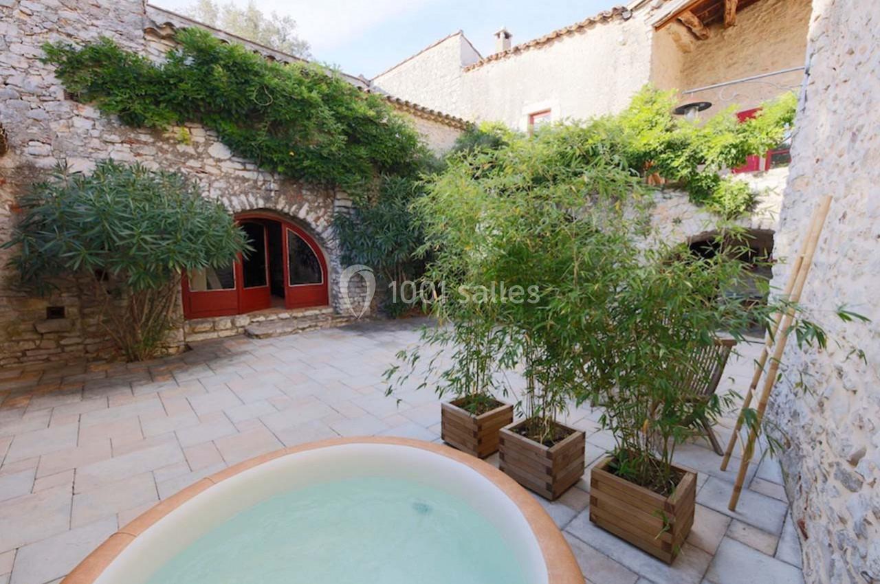 Cour intérieure en pierre avec un jacuzzi, des plantes en pots et des façades en pierre ornées de végétation.