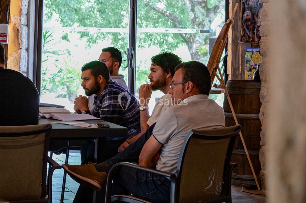 Quatre hommes assis autour d'une table, attentifs, dans une salle lumineuse avec une grande baie vitrée donnant sur des…