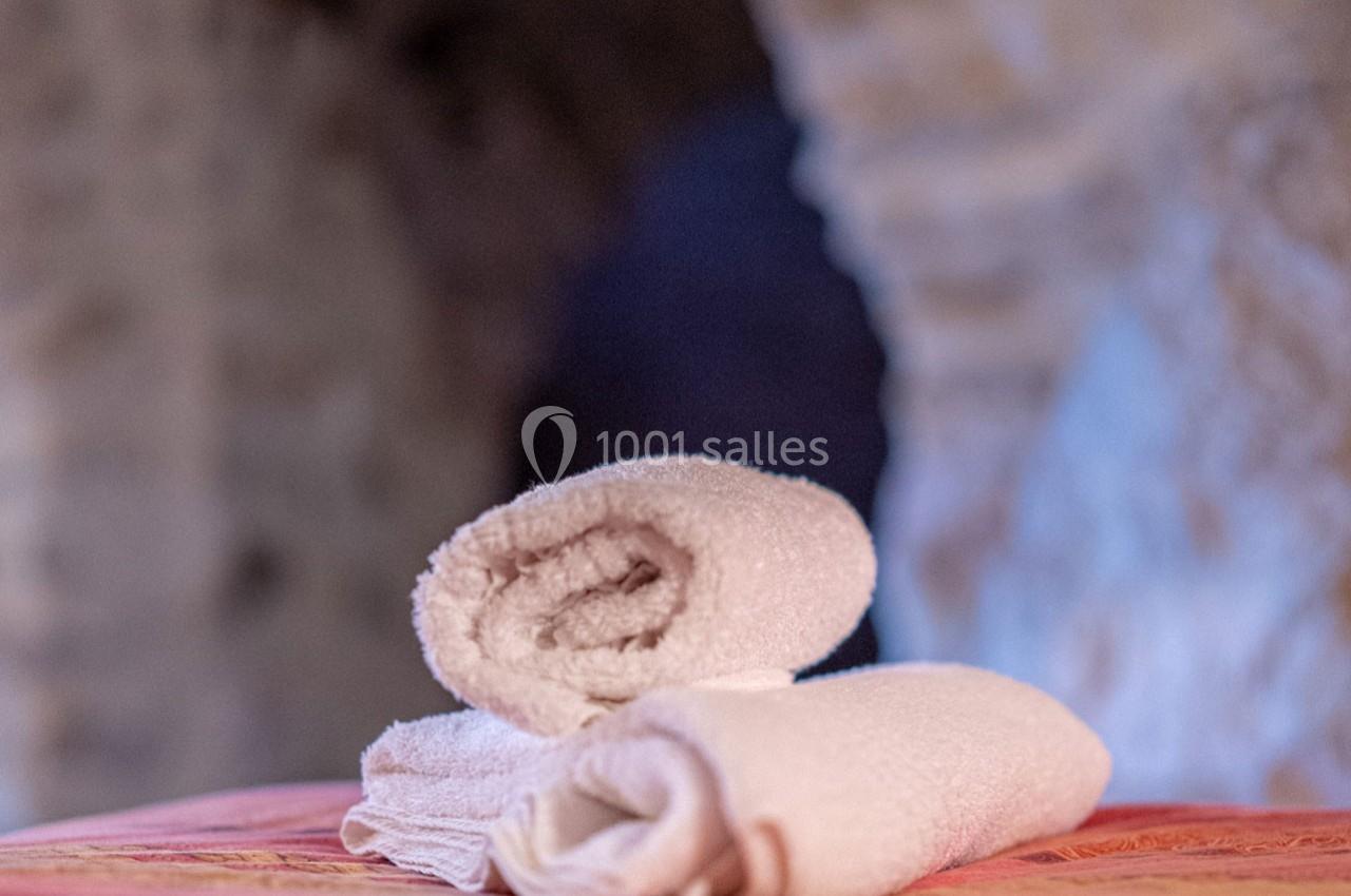 Deux serviettes blanches roulées posées sur une surface rose dans un intérieur en pierre floue en arrière-plan.