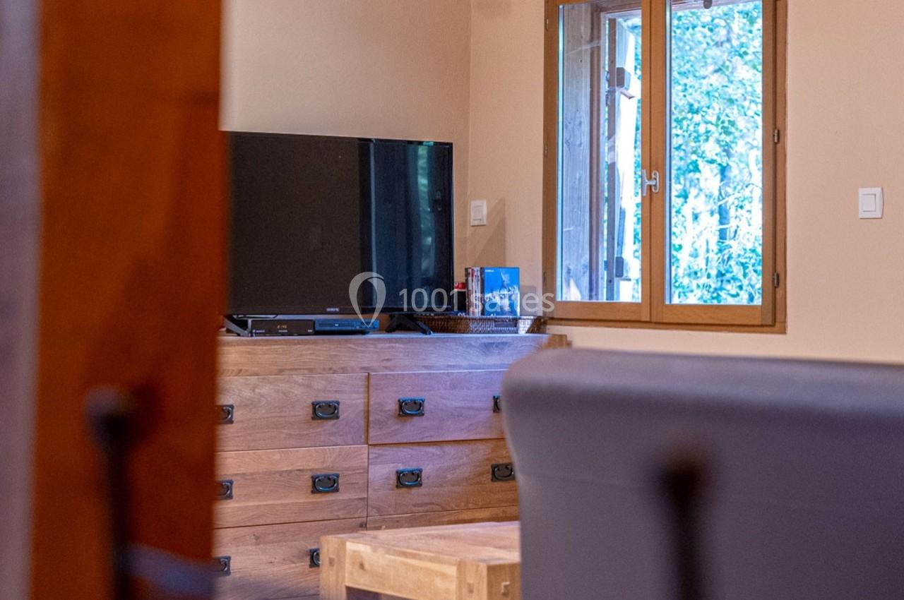 Télévision posée sur une commode en bois, près d'une fenêtre laissant entrer la lumière naturelle.