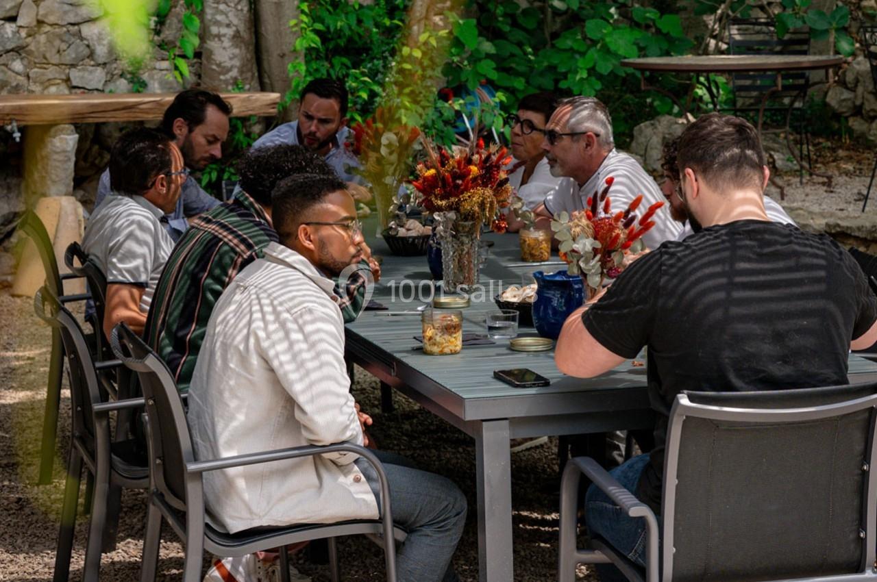 Groupe de personnes assises autour d'une table en extérieur, discutant dans un cadre verdoyant.