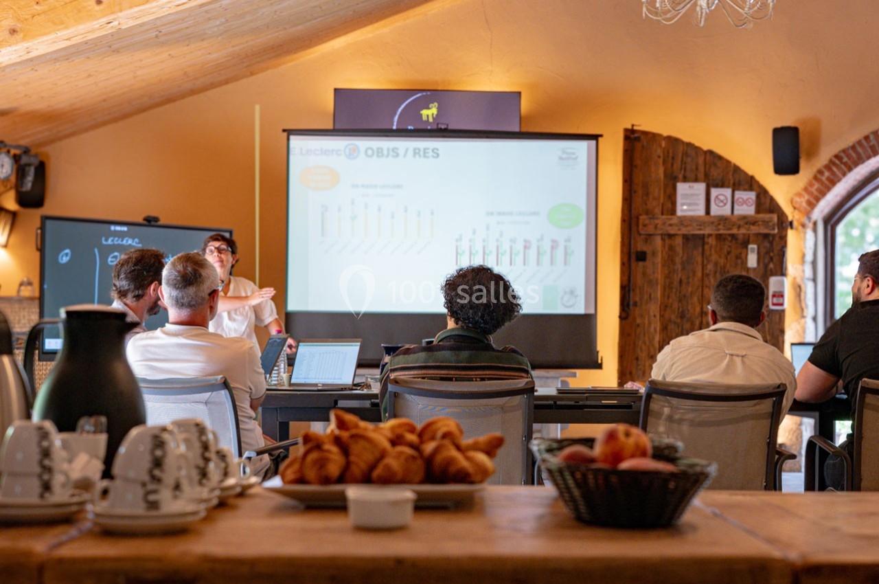 Un groupe de personnes assiste à une présentation dans une salle avec écran projeté, table en bois et viennoiseries au…