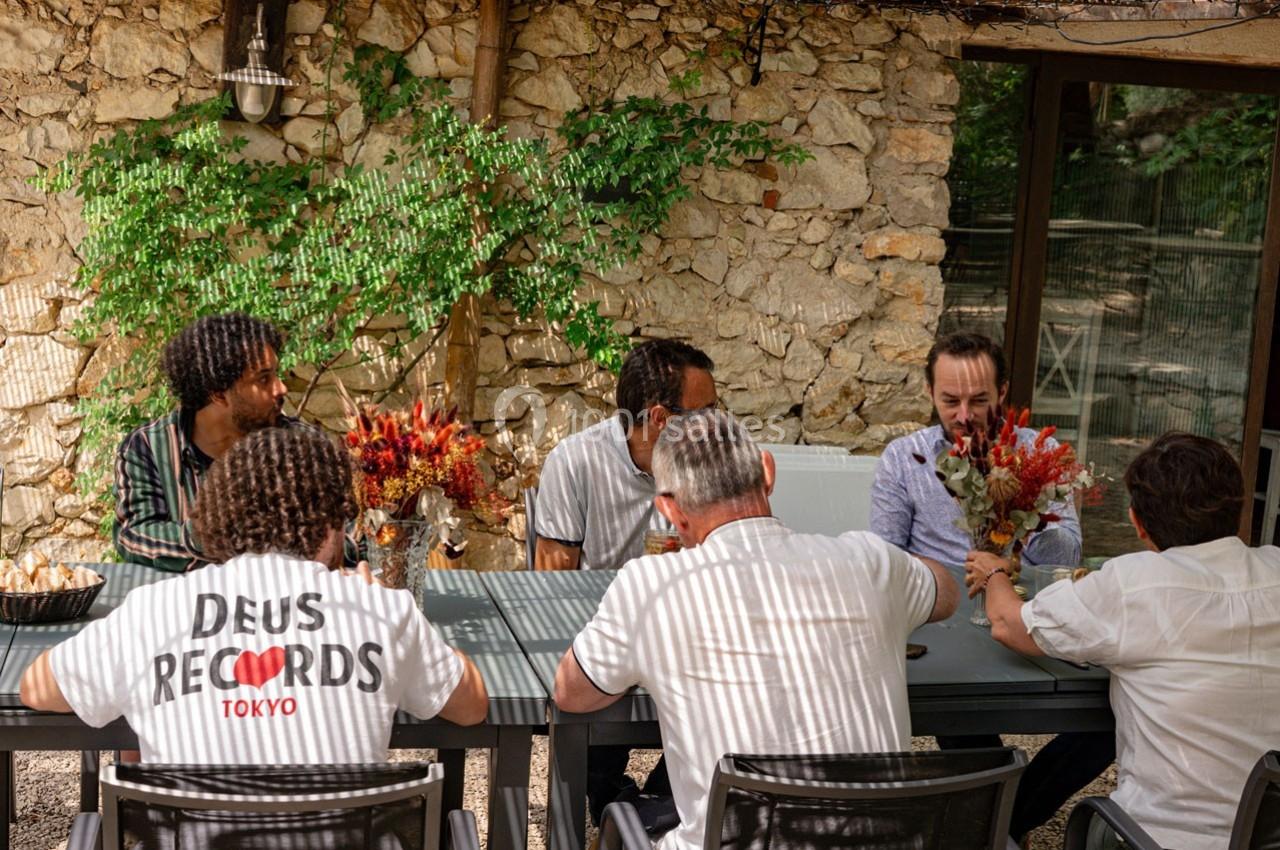 Des personnes assises autour d'une table en extérieur, discutant et tenant des bouquets de fleurs.