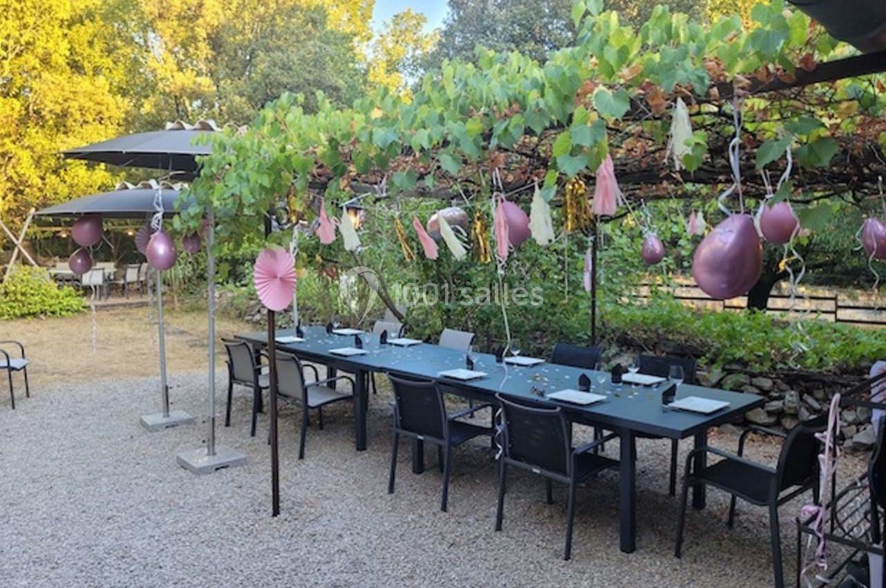 Table extérieure décorée avec des ballons et des guirlandes sous une pergola ornée de vignes, entourée de chaises.