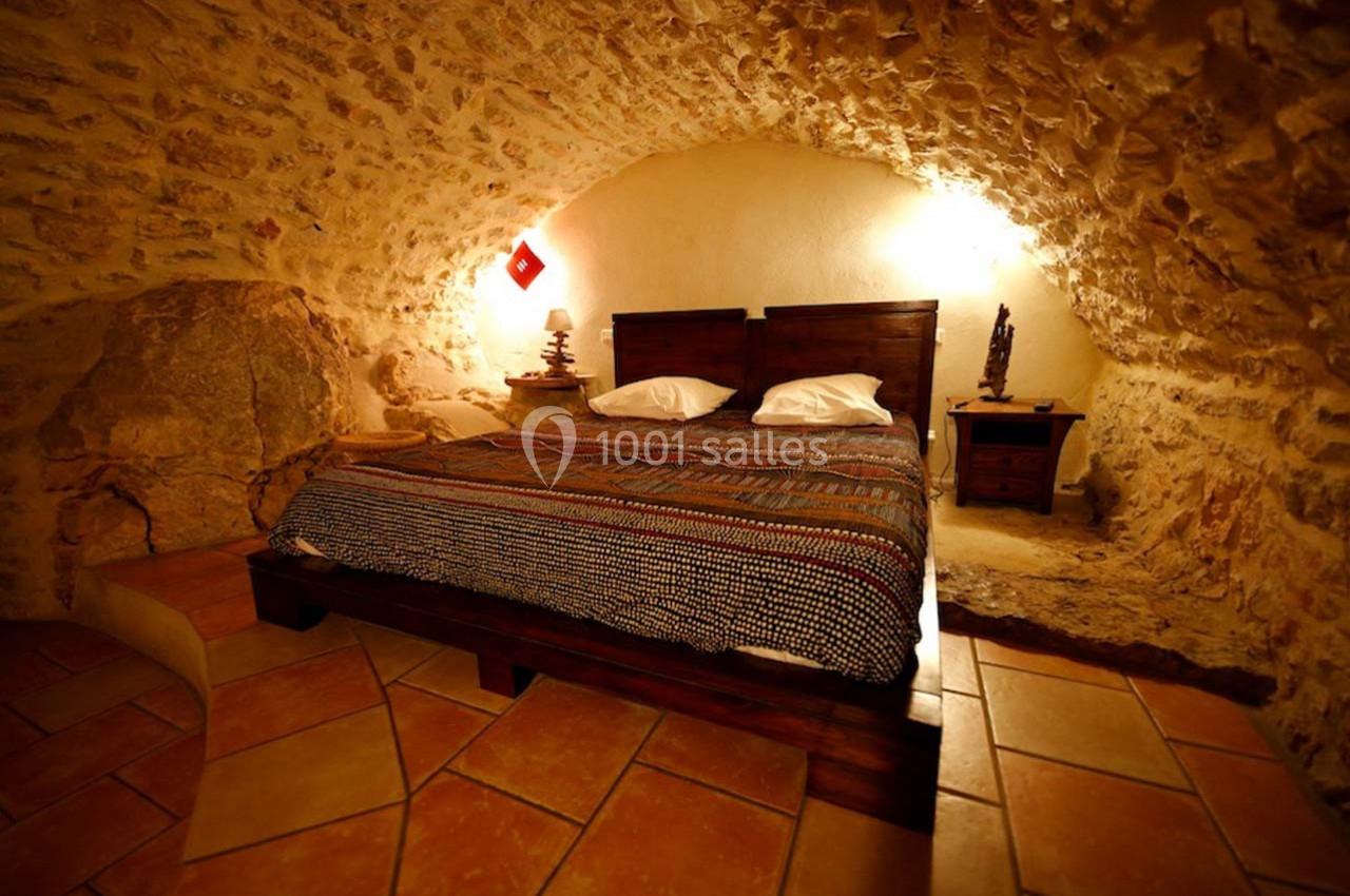Chambre rustique avec lit double, murs en pierre apparente et éclairage chaleureux dans une ambiance troglodytique.