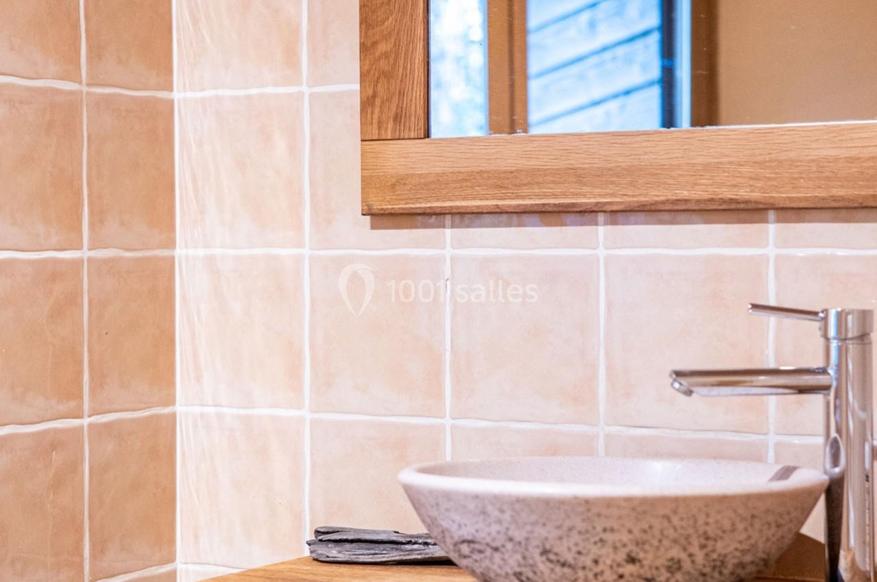 Lavabo en céramique posé sur un meuble en bois, avec un robinet métallique et un miroir encadré de bois.